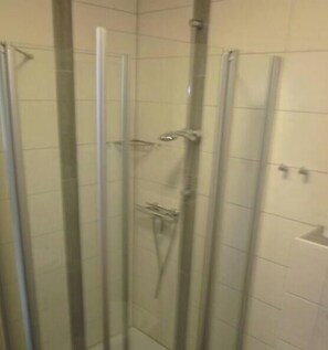 Une cabine de douche fermée par des parois en verre, dotée d’un pommeau de douche à main et d’un robinet mural.