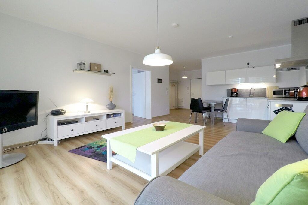 Ein modernes Wohnzimmer mit Flachbildfernseher, weißen Möbeln, einem Essbereich und einer Küche.