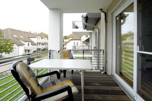 A balcony with a table and chairs, a window with a view of neighboring houses, and a metal railing. - Holiday apartment with 1 bedroom (Dierhagen)