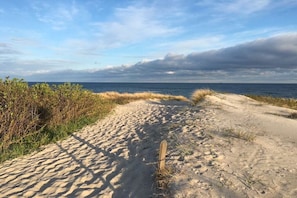 Ein sandiger Strandweg führt zum Meer unter bedecktem Himmel.
