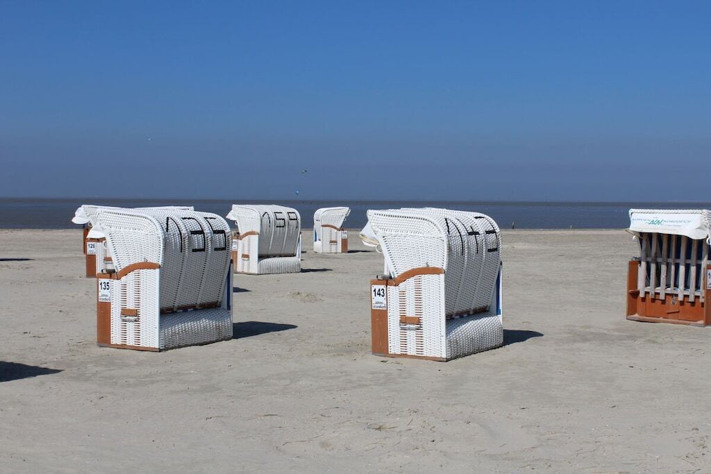 Strandliegen reihen sich an einem Sandstrand auf, im Hintergrund das Meer.