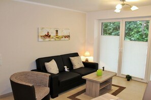 A living room with a black sofa, a small table, a lamp, and a painting on the wall. - Holiday apartment with 2 bedrooms (Norddeich)