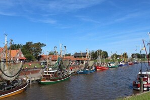 A harbor with multiple fishing boats docked, a clear sky, and buildings in the background. - Holiday apartment with 2 bedrooms (Norddeich)