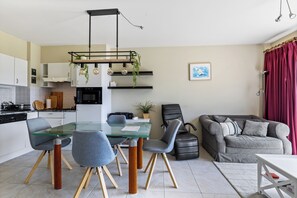 A modern kitchen with a dining area, a black leather sofa, and a red curtain. - Green Garden 9 / 0105 (De Haan)