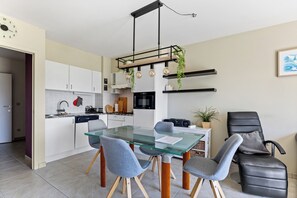 A modern kitchen with white cabinets, a glass dining table, and a black chair. - Green Garden 9 / 0105 (De Haan)