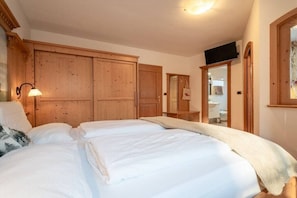 A bedroom with a large bed, wooden wardrobe, and a mirror.