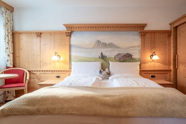 A hotel room with a bed, a red chair, two bedside tables, and a wall-mounted painting.