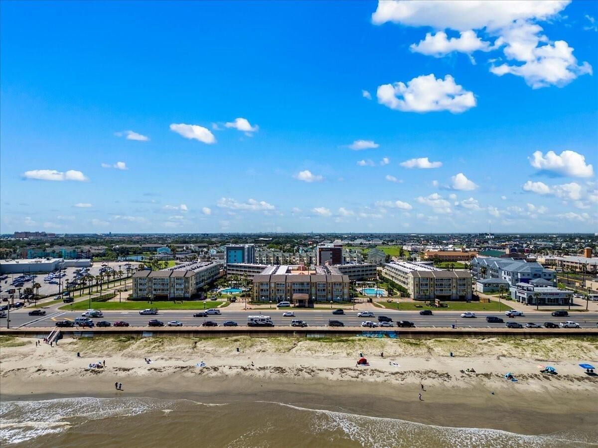 A coastal cityscape with a beachfront hotel, a large parking lot, and a clear blue sky.