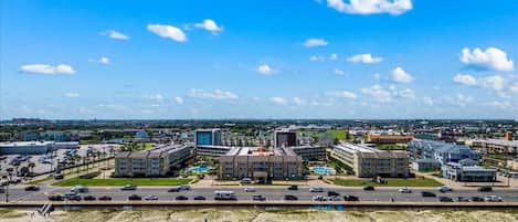 A coastal cityscape with a beachfront hotel, a large parking lot, and a clear blue sky.