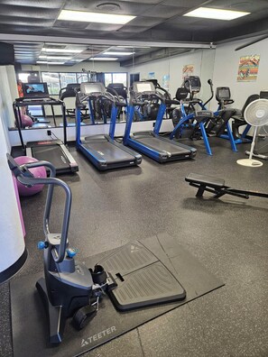 Ein Fitnessstudio mit Laufbändern, Crosstrainern und einem stationären Fahrrad.