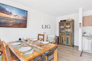 Un comedor con una mesa de madera rústica dispuesta para cuatro, un televisor que muestra una vista panorámica y un armario colorido con vajilla.