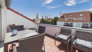 An outdoor patio area with a table and chairs, a covered umbrella, and a view of neighboring buildings. - Holiday apartment with 2 bedrooms (Langeoog)