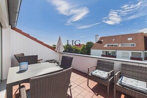 Un'area patio all'aperto con tavolo e sedie, un ombrellone e vista sui palazzi vicini.