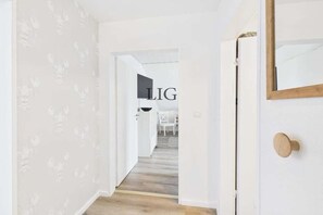 A hallway with a wooden floor, white walls, and a door with a mirror. - Holiday apartment with 2 bedrooms (Langeoog)