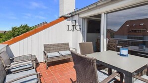 An outdoor patio with wicker furniture, a table, and a sign with 'LIG' on a white wall. - Holiday apartment with 2 bedrooms (Langeoog)