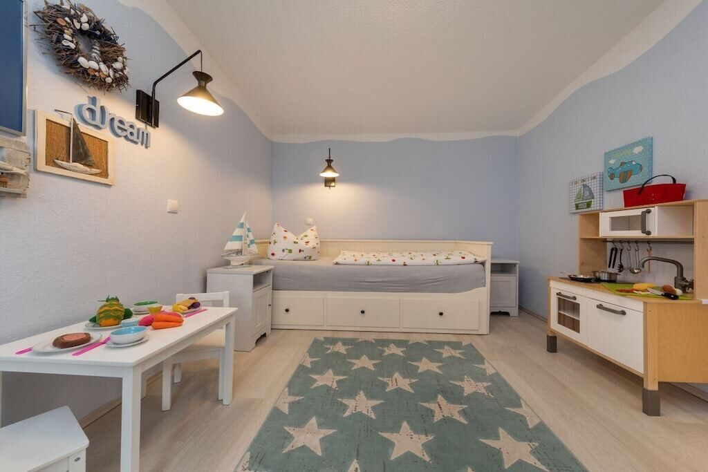 Un dormitorio infantil con cama, escritorio, una kitchenette pequeña y una alfombra con estampado de estrellas.