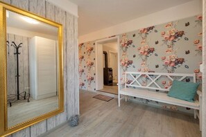 A room with a large mirror, a white bench with a cushion, floral wallpaper, and a wooden floor. - Holiday apartment in Binz with swimming pool (Binz)