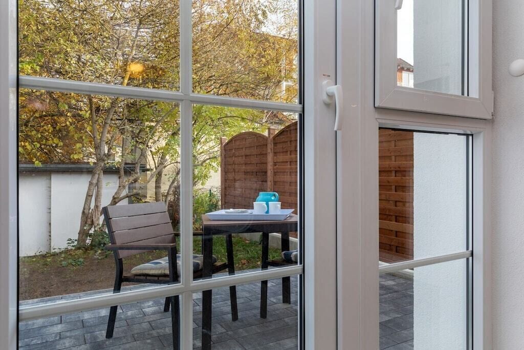 A view through a window of a patio area with a wooden fence, a table with a chair, and a brick wall.