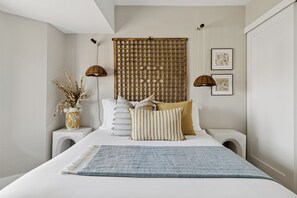 A bedroom with a bed, bedside tables, a hanging light fixture, and a wall-mounted artwork.