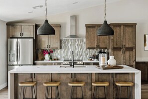 A modern kitchen with a central island, bar stools, stainless steel appliances, and pendant lighting.