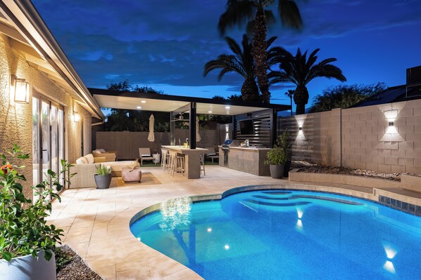 A backyard with a swimming pool, outdoor seating, and a barbecue area.