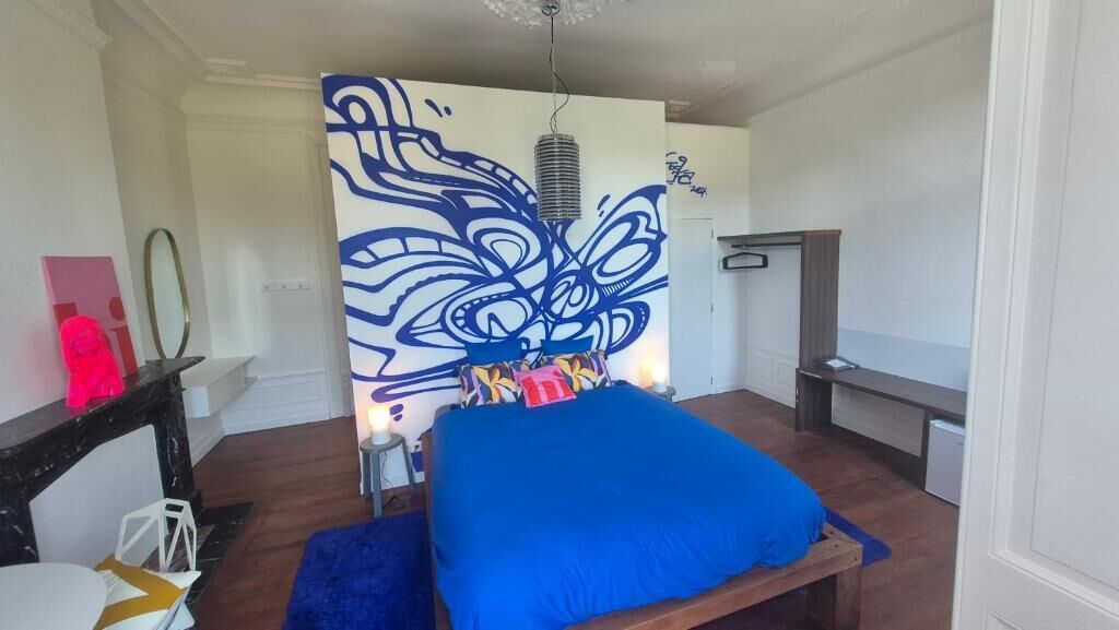Un dormitorio con cama, un mural en la pared, una mesita de noche y un velador.