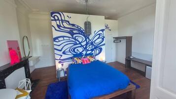 Un dormitorio con cama, un mural en la pared, una mesita de noche y un velador.