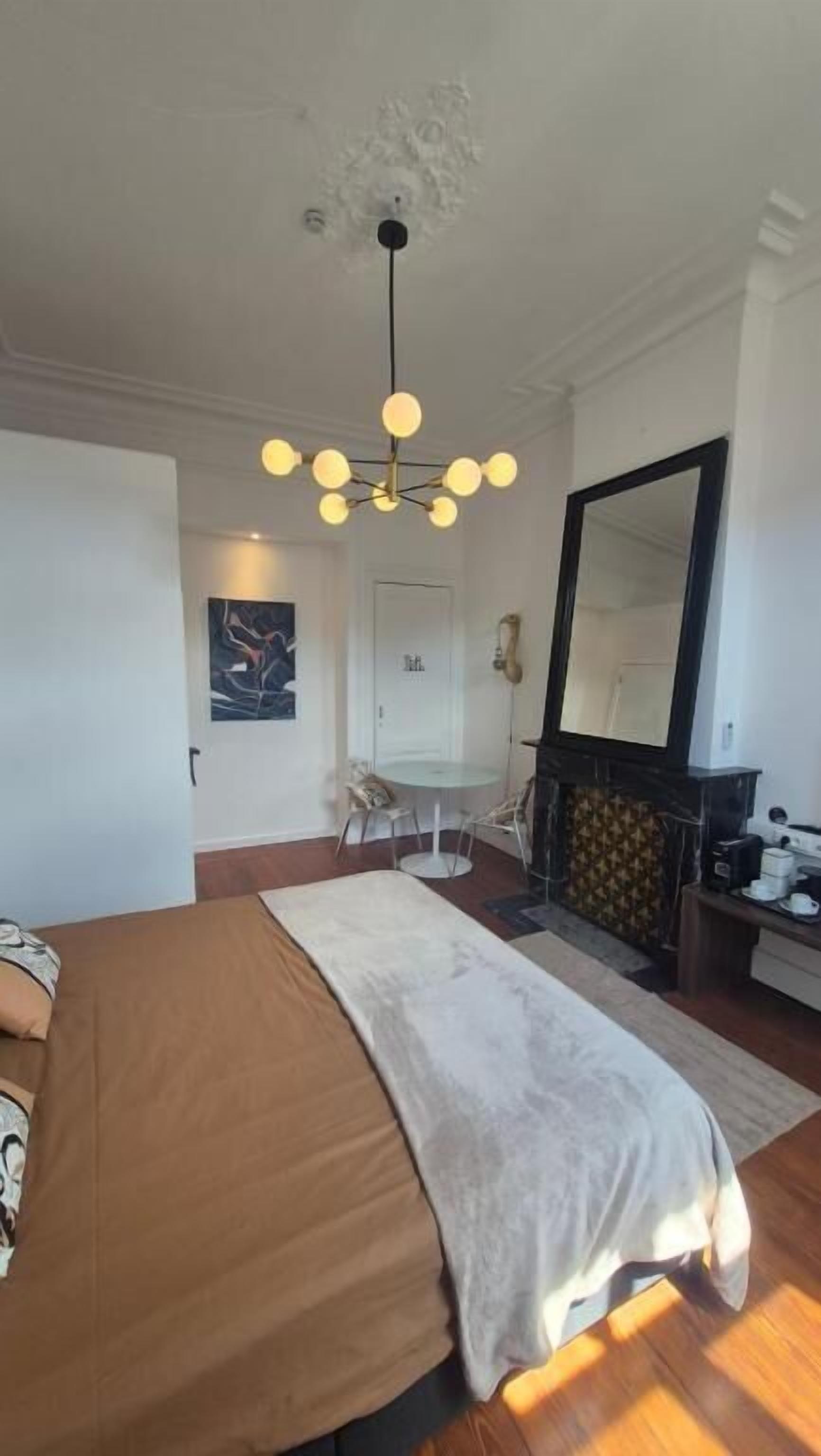 A bedroom with a bed, a chandelier, a fireplace, and a mirror.