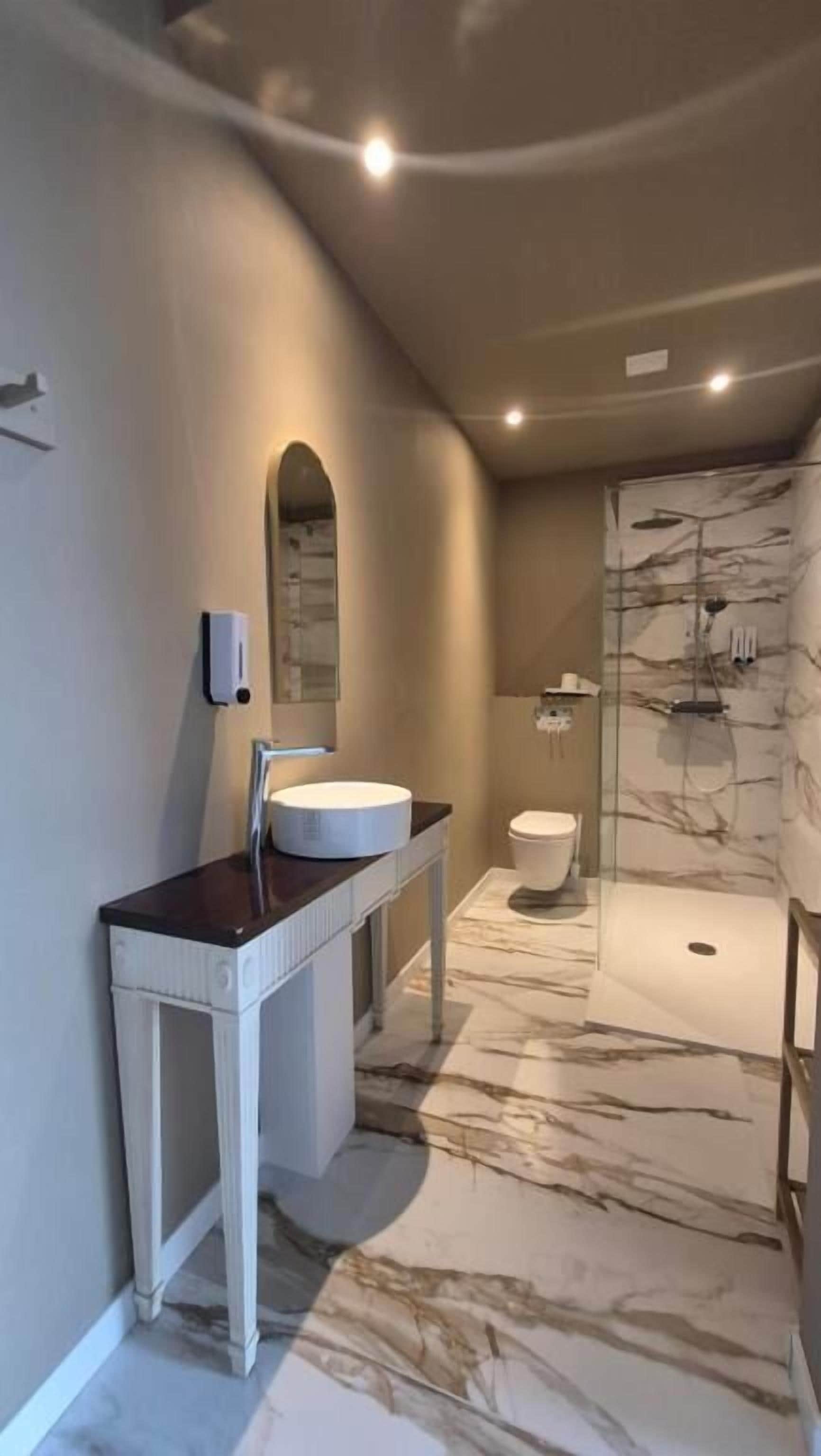 Een moderne badkamer met een marmeren vloer, een witte wastafel en een glazen douchecabine.
