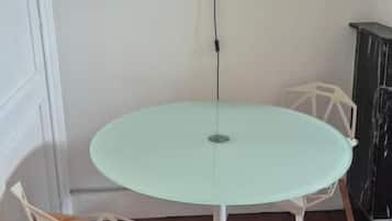 A round table with a white base, a single chair with a woven seat, and a wall-mounted light fixture.