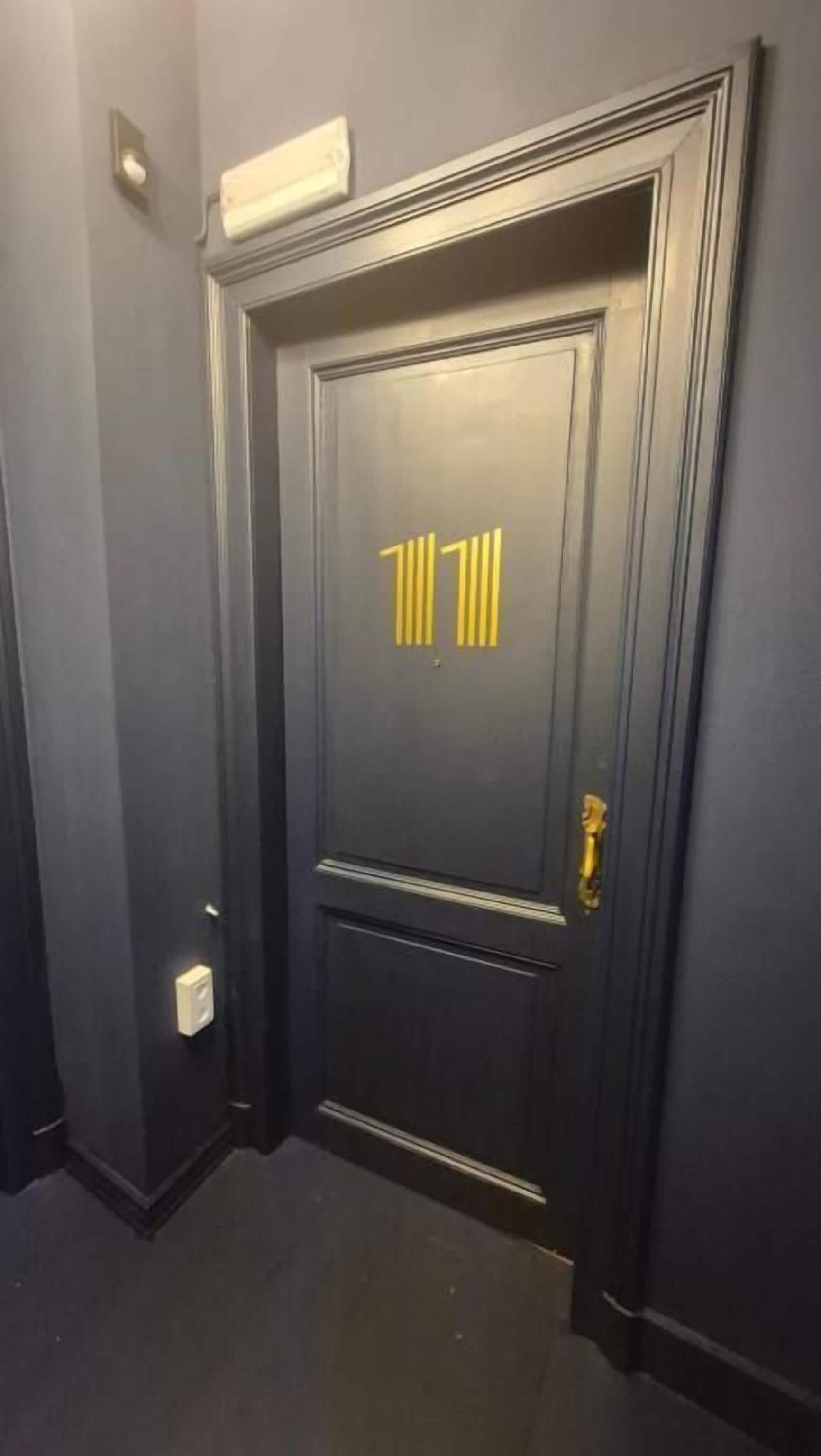 Una puerta oscura con una placa numérica dorada y un pomo de latón.