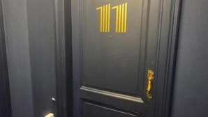 Une porte de couleur sombre, ornée d’une plaque numérotée dorée et dotée d’une poignée de porte en laiton.