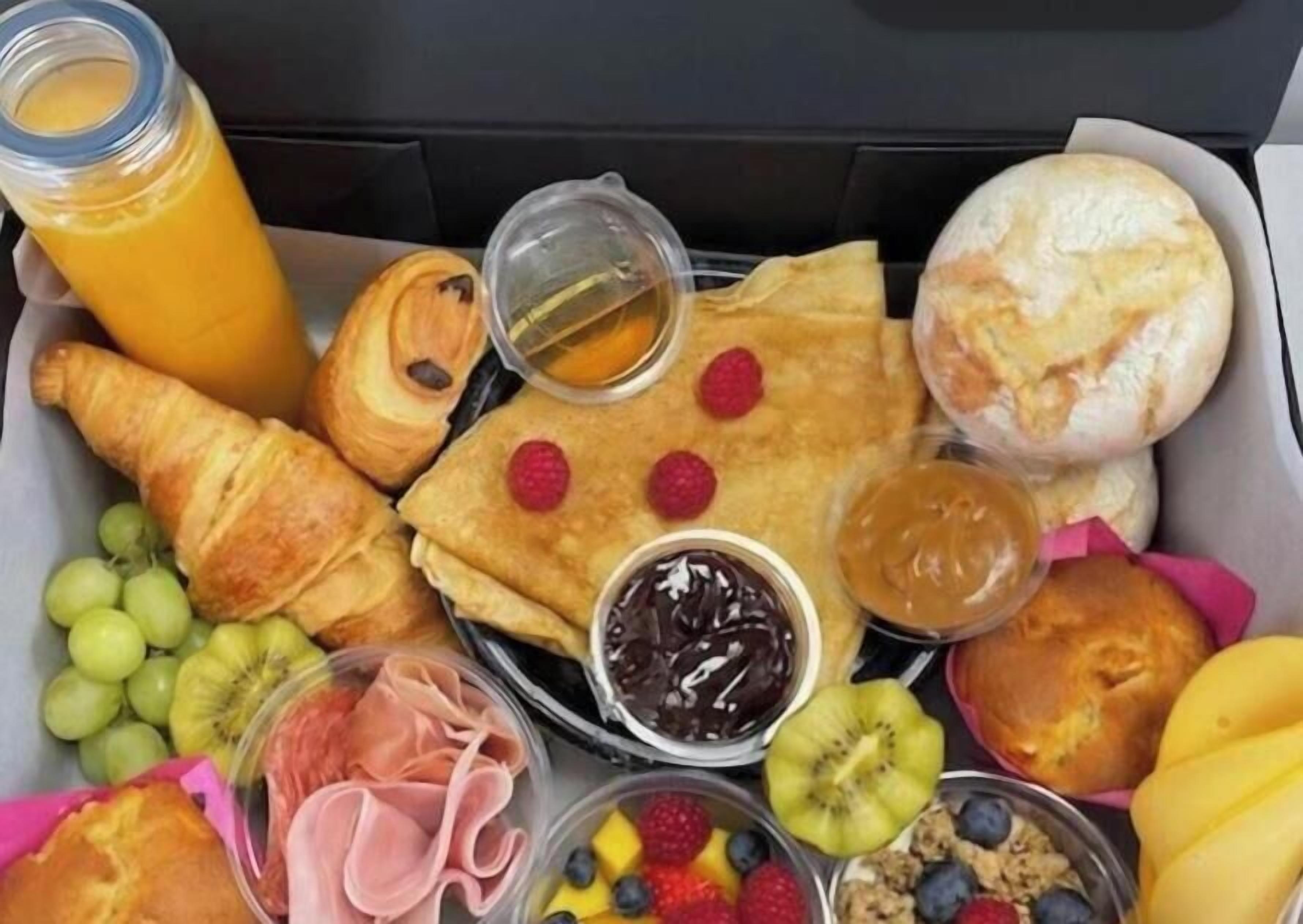 A breakfast tray with croissants, a bottle of orange juice, a pastry with raspberries, a muffin, and various fruits and spreads.