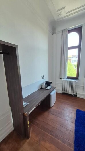 A room with a wooden floor, a bench, a radiator, and a window with curtains.