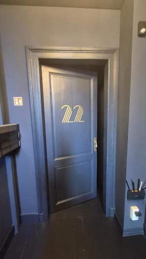 A narrow hallway with a dark wooden door featuring a gold monogram.