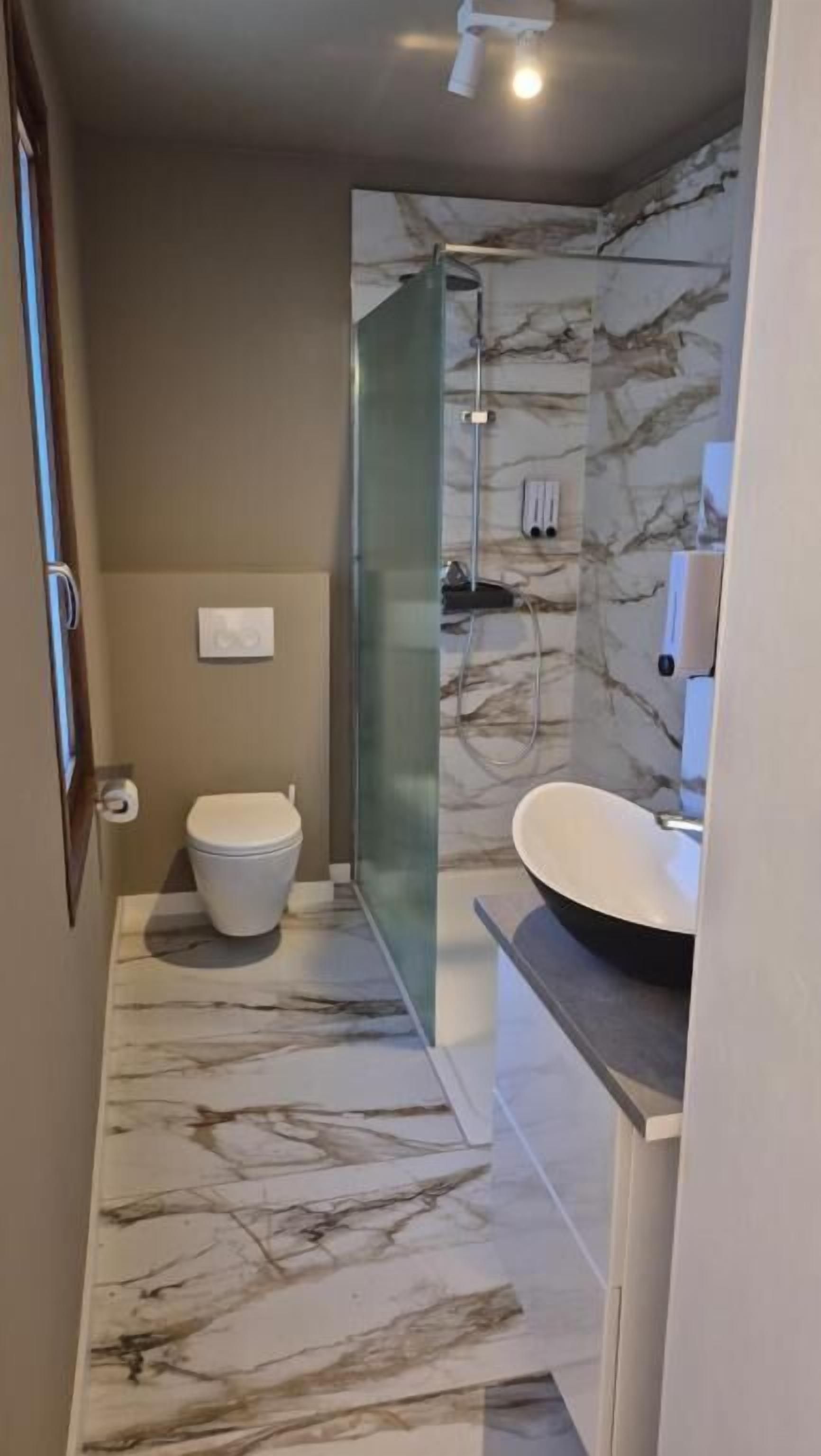 Ein Badezimmer mit Marmorboden, Toilette, Duschkabine aus Glas und Waschbecken.