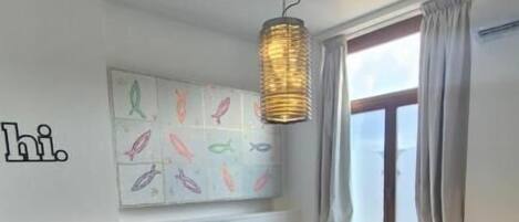 Un dormitorio con cama, un tapete azul, una pared con obras de arte, una lámpara colgante y una ventana con cortinas.