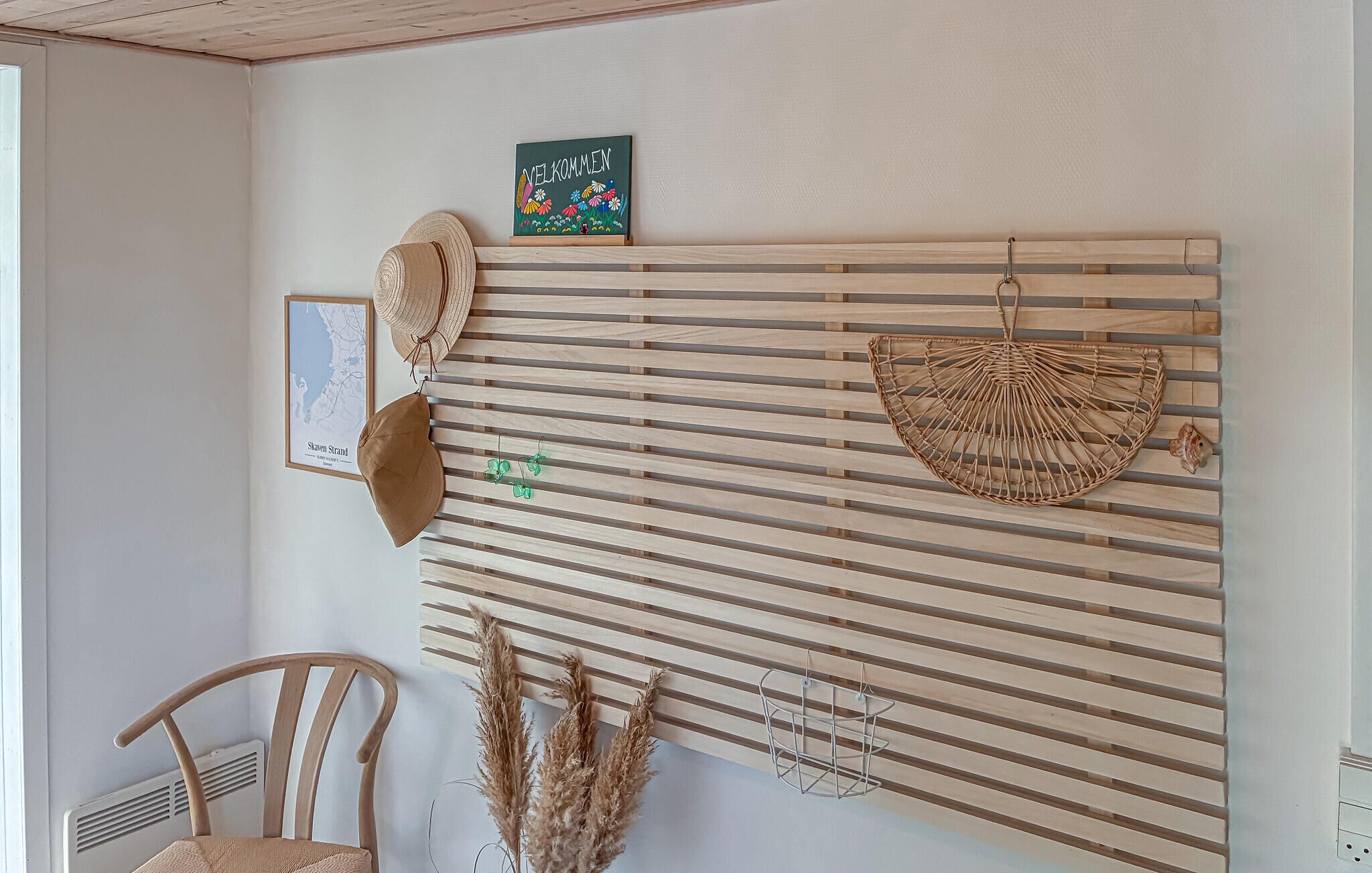 A room with a wooden slat wall, a framed map, a welcome sign, a hat, a chair, and dried plants.
