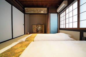 Ein traditioneller japanischer Raum mit Tatami-Böden, einem Bett mit floralem Überwurf, einem Shoji-Bildschirm und einem an der Wand hängenden Kunstwerk.