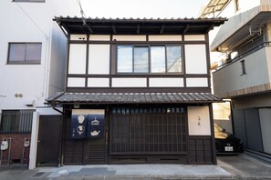 Ein traditionelles japanisches Gebäude mit einem Ziegeldach, Holzschiebetüren und einem kleinen Vordach mit hängenden Gegenständen.