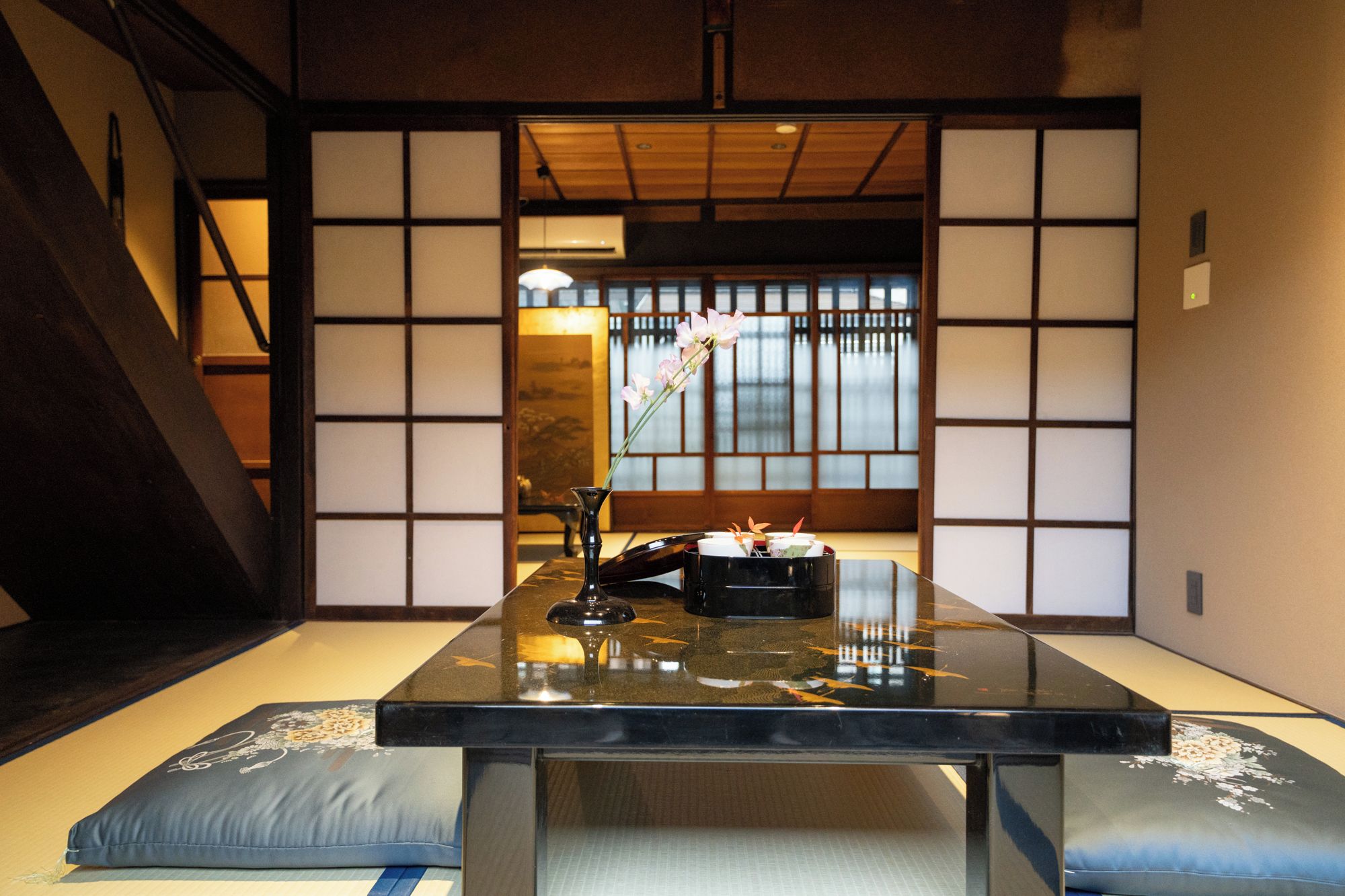 A traditional Japanese room with tatami flooring, a low table with a black surface, and a sliding door with a view of a garden.