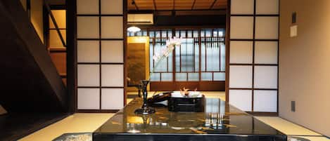 Una habitación tradicional japonesa con suelo de tatami, una mesa baja con superficie negra y un puertas correderas con vistas a un jardín.