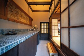 Un couloir étroit avec un mur recouvert de carreaux, un banc en bois et une porte coulissante traditionnelle.