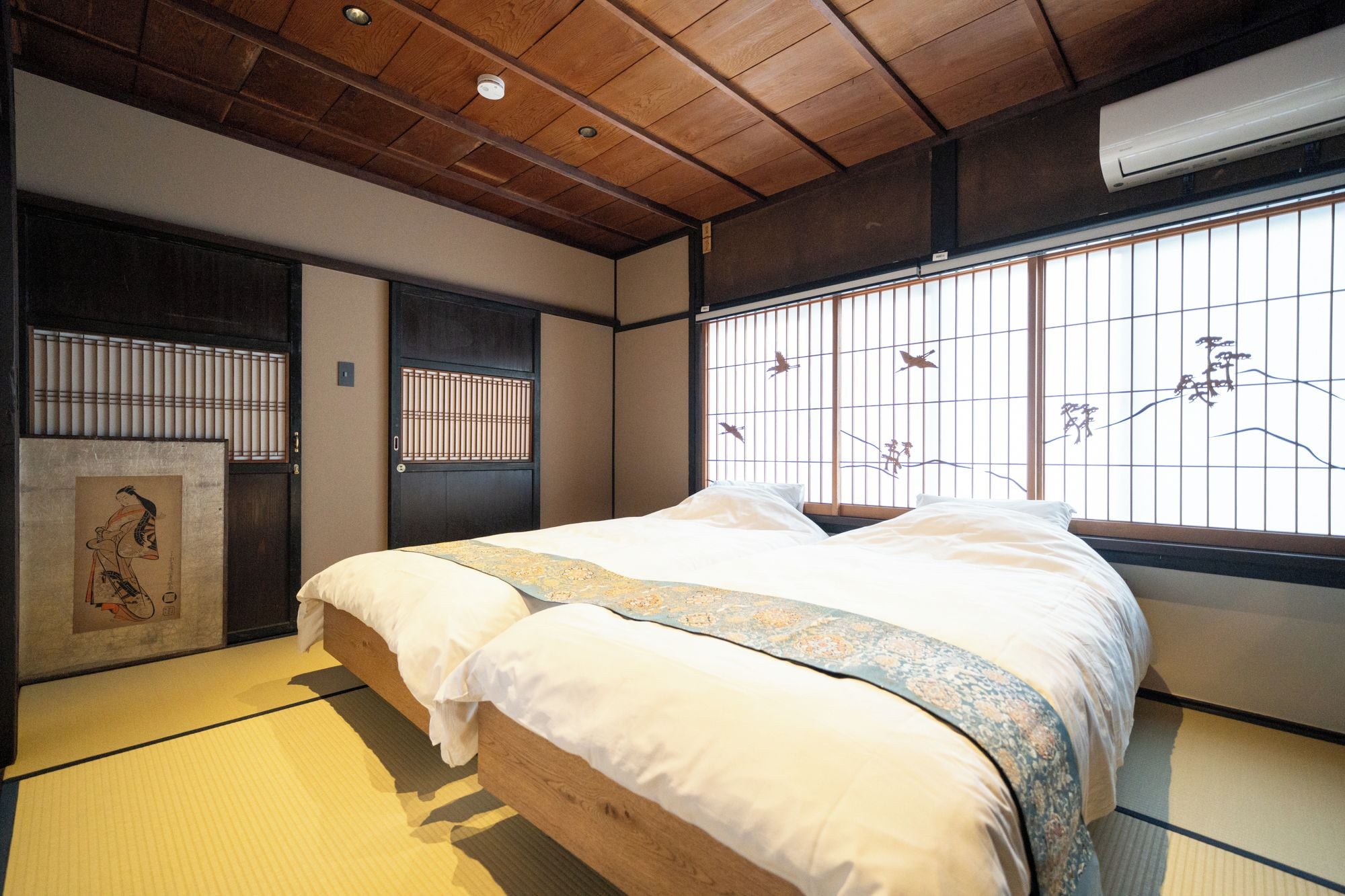 A traditional Japanese-style room with tatami flooring, a wooden bed, a shoji screen with a bird mural, and a sliding door.