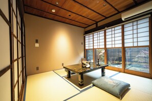 Une pièce de style japonais traditionnel, avec un sol recouvert de tatamis, une petite table basse avec un coussin et une vue à travers des panneaux coulissants en papier.