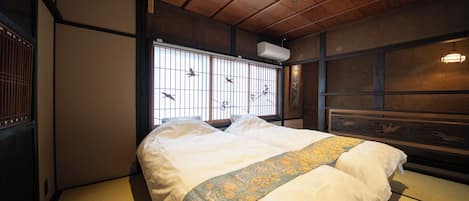 Um quarto japonês tradicional com tatames, uma cama com colcha estampada, janela com vista para pássaros e teto de madeira.
