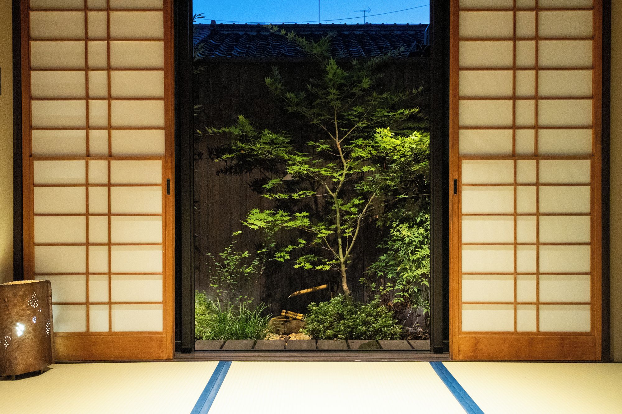 A traditional Japanese room with tatami flooring, a shoji screen door, and a bonsai tree.