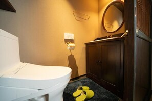 A bathroom with a toilet, a wooden cabinet, a mirror, and a pair of yellow slippers on the floor. - Kokeiran Kyoto Machiya (Kyoto)