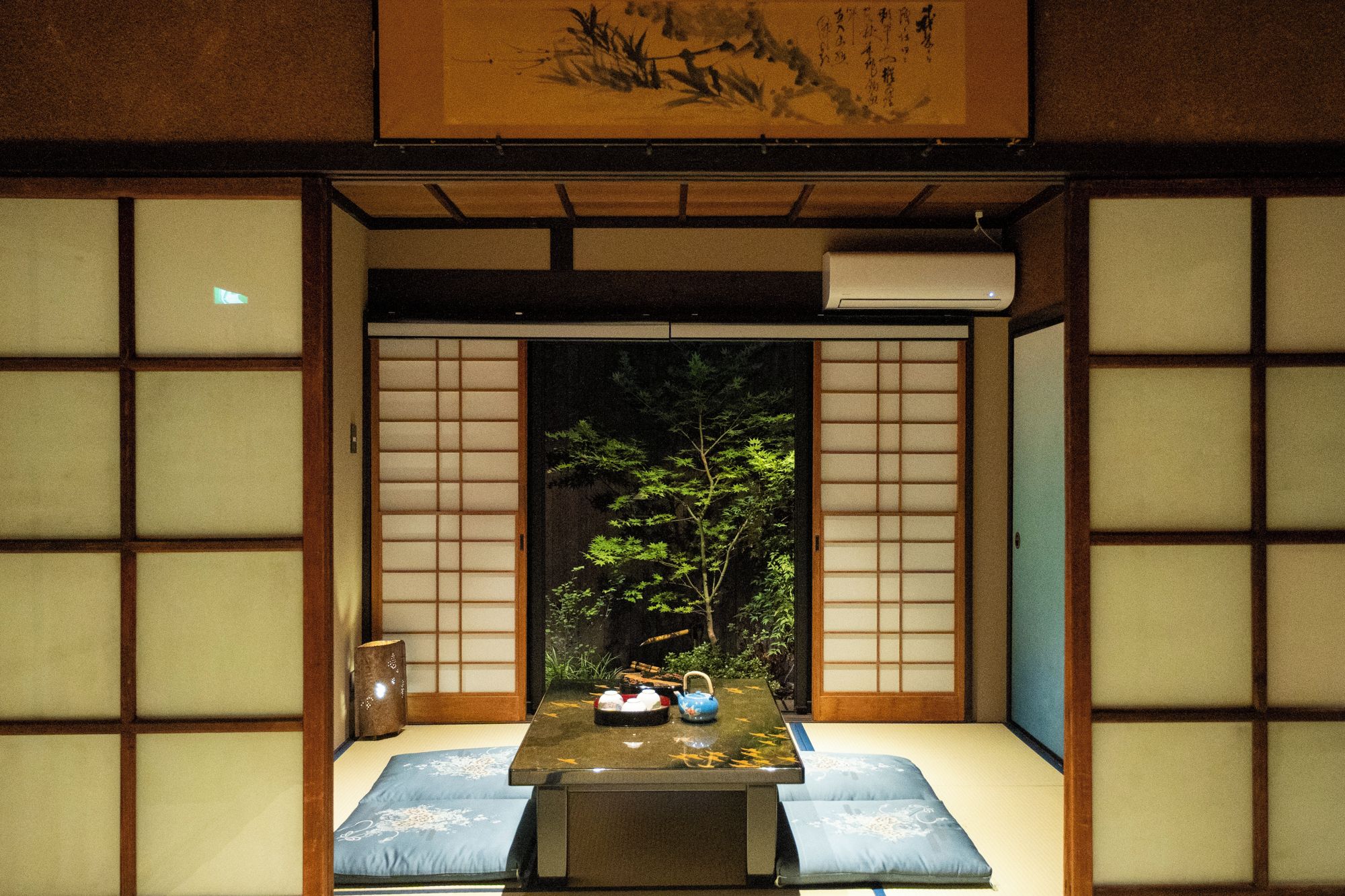 A traditional Japanese room with tatami flooring, shoji screens, and a low table with a blue cushion.