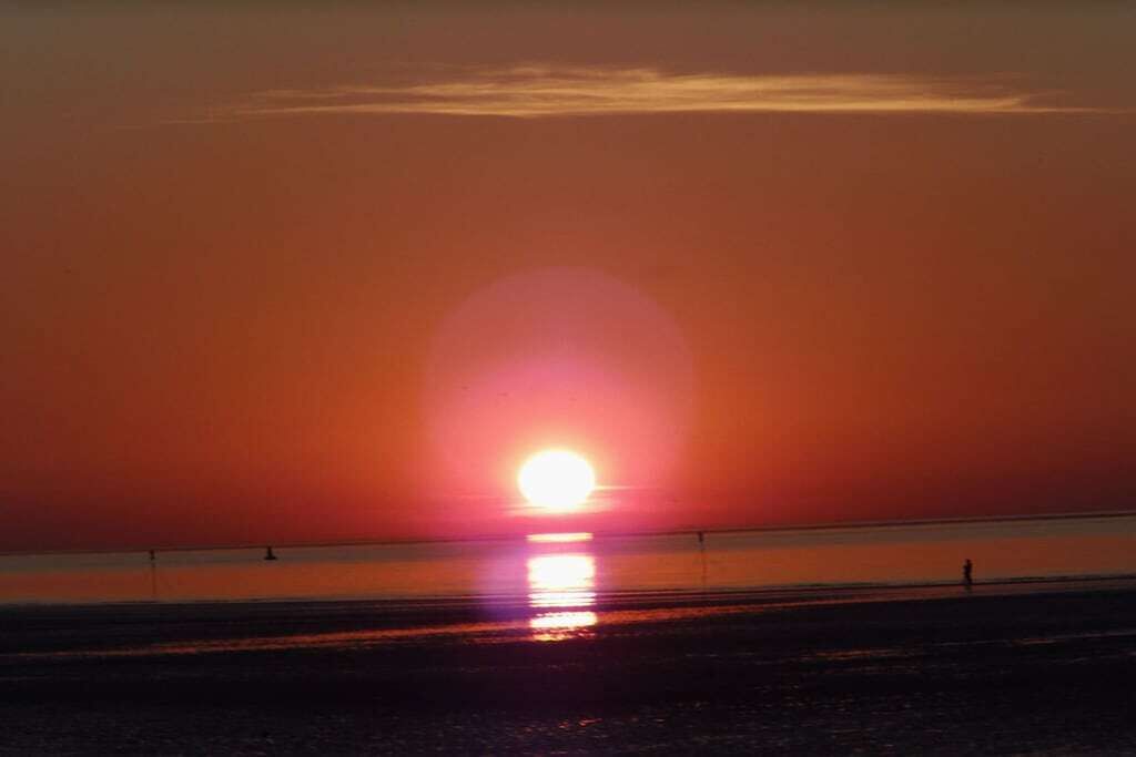 Ein Sonnenuntergang über einem Strand mit ruhiger See, und eine einzelne Person geht am Ufer entlang.